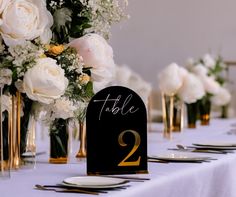 the table is set up with white flowers and gold place settings for two people to sit at