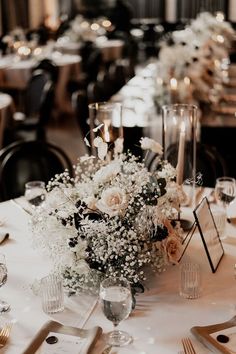 the table is set with silverware and white flowers in vases, candles and napkins