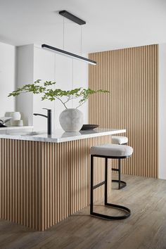 a modern kitchen with wooden paneling and white counter tops, stools and a plant in the center