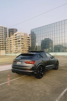 a black car parked in a parking lot next to tall buildings with windows on each side