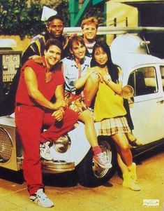 a group of young people posing for a photo in front of an old fashioned car