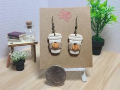 a pair of earrings with pumpkins on them sitting in front of a small card