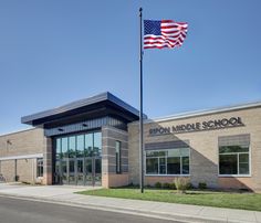 an american flag flying in front of a school building with windows and grass on the sidewalk