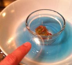 a finger pointing at a small glass filled with liquid on top of a white plate