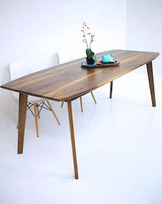 a wooden table with two white chairs and a flower vase on it, in front of a white wall