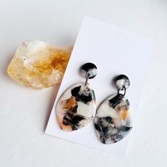 a pair of earrings sitting on top of a piece of paper next to a rock