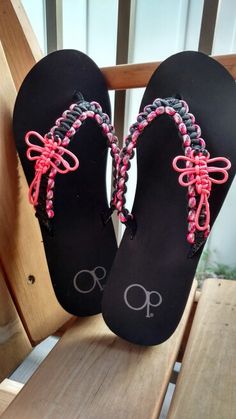 a pair of black sandals with pink and grey beads on them sitting on a wooden chair