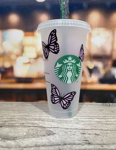 a starbucks cup with butterflies painted on the side sitting on a wooden table in front of a blurry background