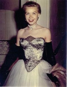 an old photo of a woman in a white and black dress smiling for the camera