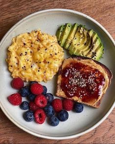 a white plate topped with eggs, toast and berries on top of a wooden table