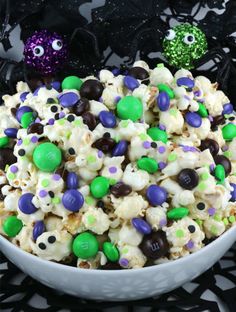 a white bowl filled with halloween popcorn next to two green and purple candies on a black table