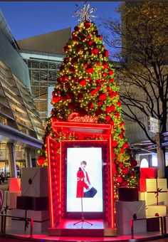 a lighted christmas tree in the middle of a shopping mall with presents around it and an ad for coca - cola