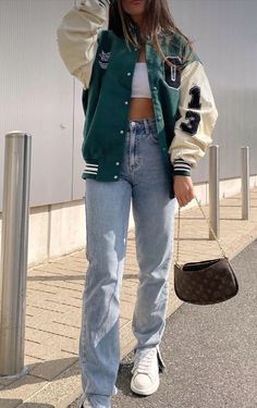 a woman standing in front of a building wearing a green jacket and white crop top