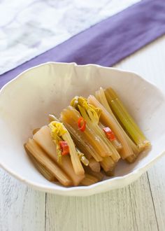 a white bowl filled with pickles on top of a wooden table next to a purple napkin