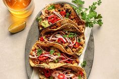 three tacos on a plate with cilantro, onions and other toppings