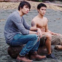 two young men sitting next to each other on top of a rock in the sand