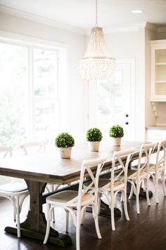 a dining room table with white chairs and two potted plants on top of it