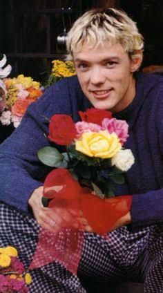 a young man sitting on the ground holding a bouquet of roses and a red ribbon