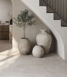 two vases sitting next to each other in front of a stair case with a potted plant