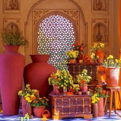 vases and flowers are arranged in front of a wall with an arched window behind them