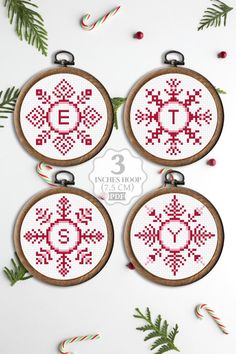 three cross stitch christmas ornaments with candy canes on the side and evergreen branches around them