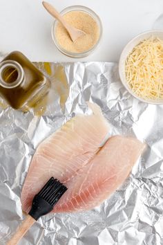 raw fish fillets on aluminum foil with grated cheese and seasoning in bowls