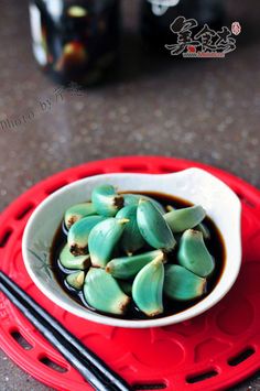 a white bowl filled with green vegetables next to chopsticks on a red tray