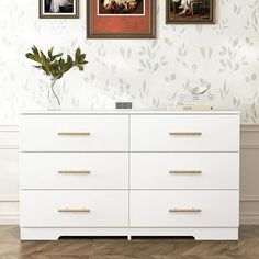 there is a white dresser with two pictures on the wall