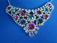 This is a very pretty vintage silver bib necklace with colourful CZ stones. It measures 18 inches in total and has an extender chain of 3 inches. The jewel encrusted bib measures 4 inches across and 2 inches from top to bottom. The vey colourful 'bib' is encrusted with sparkling imitation diamonds and sparkling CZ amethysts, sapphires and rubies. Each colourful stone lies at the centre of a  flower design of 'diamonds'. This is a spectacular and now rare piece of costume jewellery which will look stunning against any skin tone or dark dress and is sure to bring many compliments. It sparkles gloriously and spectacularly in both sunshine and artificial light and would glitter wonderfully in candlelight ! Whenever and however you choose to wear this delightful necklace, it is sure yo be a top Multicolor Rhinestone Wedding Necklaces, Multicolor Rhinestone Necklaces For Weddings, Multicolor Rhinestones Necklace For Wedding, Multicolor Rhinestone Necklace With Jewels, Costume Jewelry, Silver Multi-stone Necklace For Parties, Multicolor Rhinestone Necklace Costume Jewelry, Multicolor Rhinestone Costume Necklace, Multicolor Crystal Rhinestone Costume Necklace, Multicolor Crystal Rhinestone Necklace