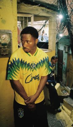 a man standing in front of a yellow wall wearing a green and blue shirt with an eagle on it's chest