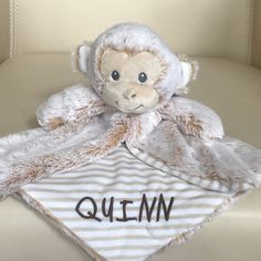 a stuffed monkey sitting on top of a white and brown blanket with the word qum written on it