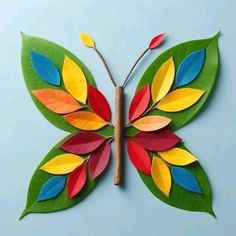 a paper butterfly with colorful leaves on it's wings, sitting on a blue surface