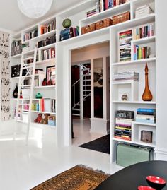 a living room filled with lots of white furniture and bookshelves on the wall