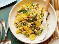 a white bowl filled with corn on top of a table next to utensils