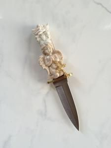 a knife with some flowers on it sitting on a marble counter top next to a white wall