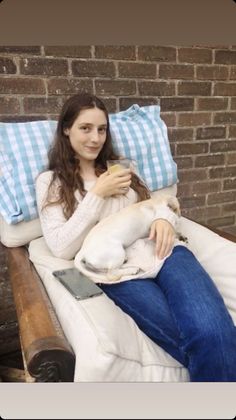 a woman is sitting on a bed with her dog and drinking from a glass in front of her