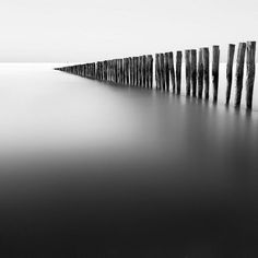 a black and white photo of a long wooden fence on the water's edge