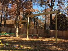 an empty yard with a wooden swing set in the foreground and lots of leaves on the ground