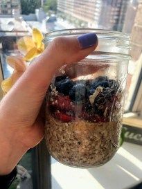 a person holding up a jar filled with granola and blueberries on top of a window sill