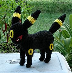 a crocheted black cat with yellow eyes standing on top of a cement slab