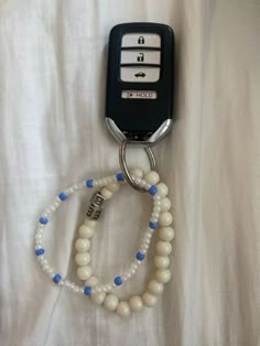 a white beaded keychain with blue beads and a black cell phone attached to it