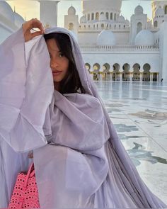 a woman in a white dress is holding her hand over her head and looking off into the distance