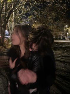 two people sitting on a park bench at night with trees in the background and one person holding another