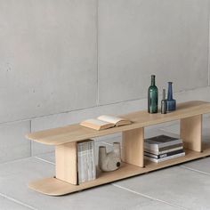 a wooden table with books and vases on the top, in front of a concrete wall