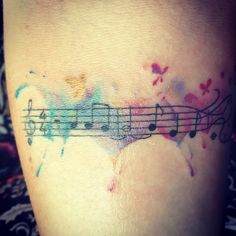 a tattoo with musical notes painted on it's side and watercolor splashes