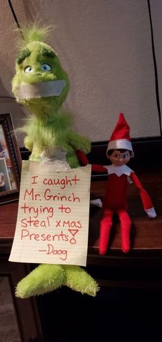 an elf holding a sign that says i caught mr grin trying to steal xmas presents day