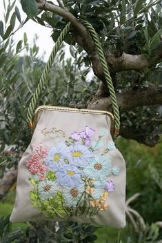 a purse hanging from a tree branch with flowers painted on the front and side of it