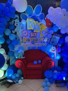 a birthday party with balloons and decorations on the wall, including a red chair in front of a blue balloon arch