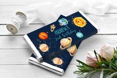 an open book with planets on it next to flowers and a roll of toilet paper