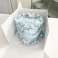 a blue cake in a white box with butterflies on the top and numbers on the bottom